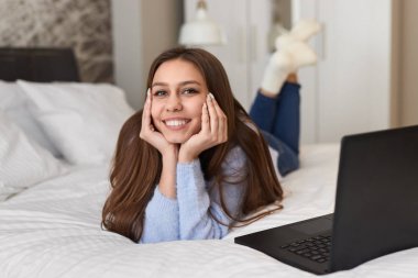 Dizüstü bilgisayarın yanında yatakta neşeli genç kadın