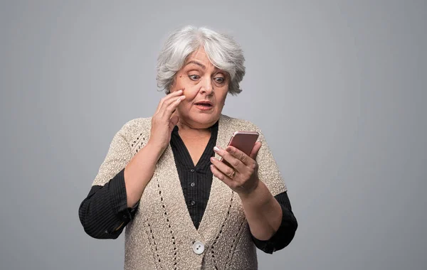 Шокированная пожилая женщина с помощью смартфона — стоковое фото
