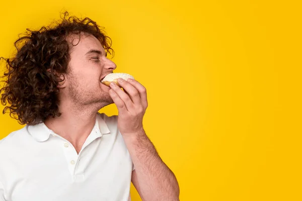 Junger Mann beißt leckeren Donut — Stockfoto