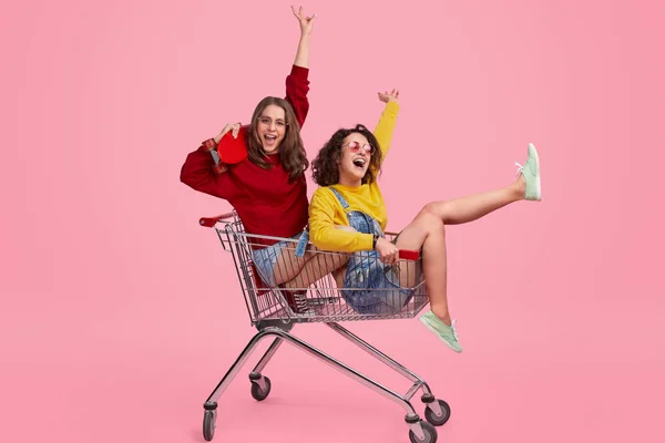 Cheerful sisters riding shopping trolley — Stock Photo, Image