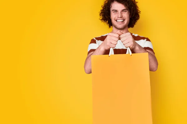 Smiling guy presenting bright paper bag — Stock Photo, Image