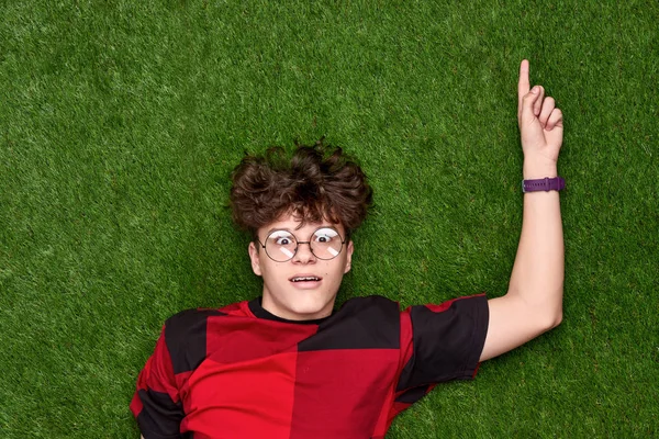Zdumiony nastolatek chłopiec wskazując na trawie — Zdjęcie stockowe