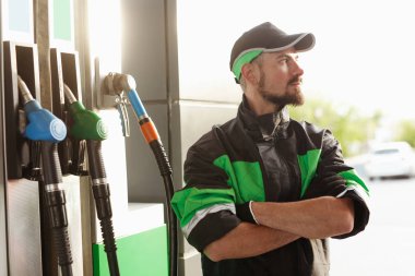 Kendinden emin dolum istasyonu çalışanı uzağa bakıyor