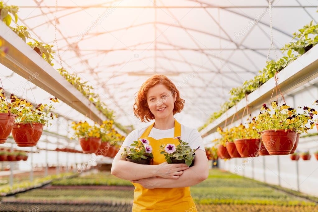 Smiling lady with potted flowers in hothouse