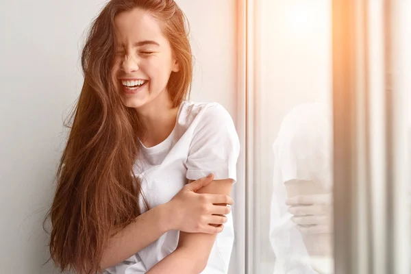 Jonge vrouw lachend in de buurt van venster — Stockfoto