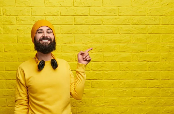 Веселий хіпстер, що вказує на жовту стіну — стокове фото