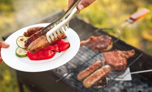 Couper la main en mettant des saucisses grillées sur l'assiette — Photo