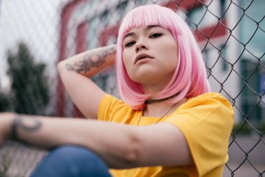 Asyalı hipster çit yakınında oturan