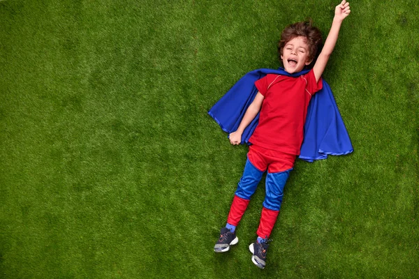 Lycklig liten superhjälte liggande på gräs — Stockfoto