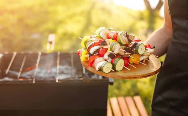 Безликий повар с овощами на деревянных палочках для гриля

