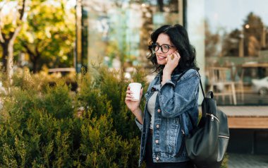 Sokakta telefonda sohbet ederken kahve içen sıradan kadın