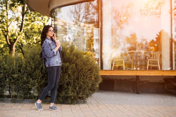 Jolie jeune femme dans des lunettes parlant au téléphone tout en marchant le long de la rue — Photo