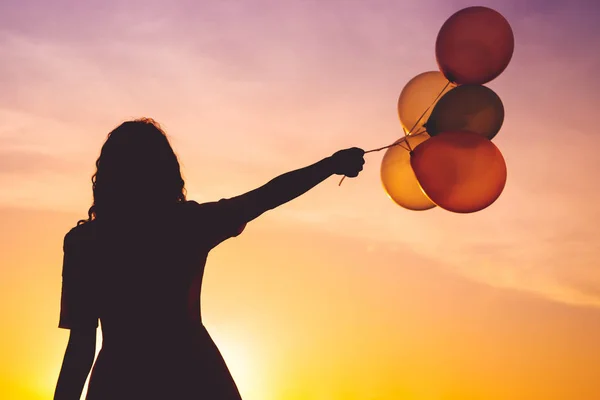 Drömmande kvinna som transporterar flygande ballonger på färgglada solnedgång — Stockfoto