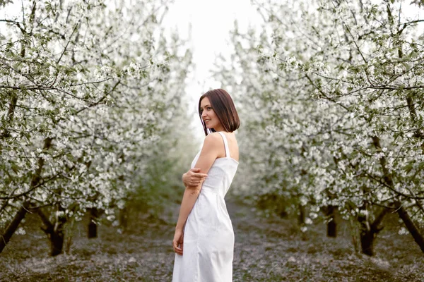 Konten wanita modern dalam berpakaian berdiri di taman musim semi mekar — Stok Foto