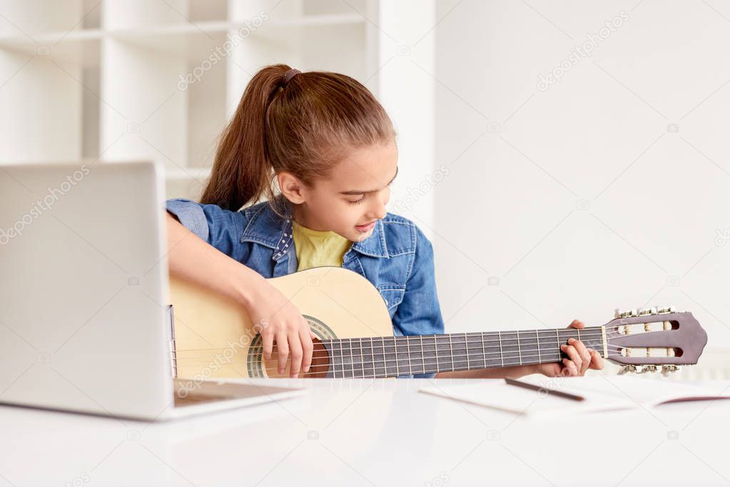 Focused girl self-learning playing guitar using laptop