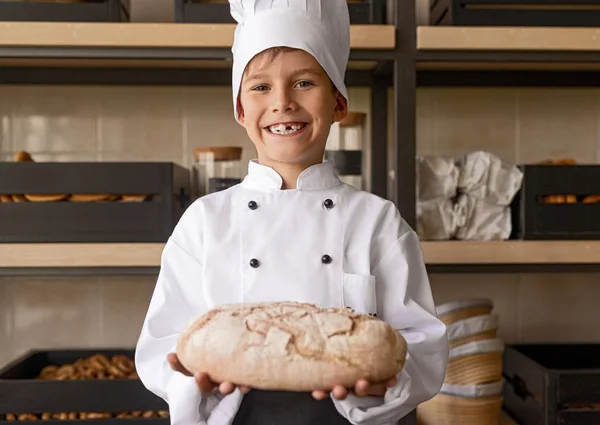 Гордий маленький пекар у формі, що тримає свіжу випічку, стоячи у пекарні — стокове фото