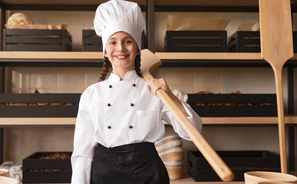 Orgulloso panadero en uniforme sosteniendo utensilio de madera mientras está de pie en la panadería —  Fotos de Stock