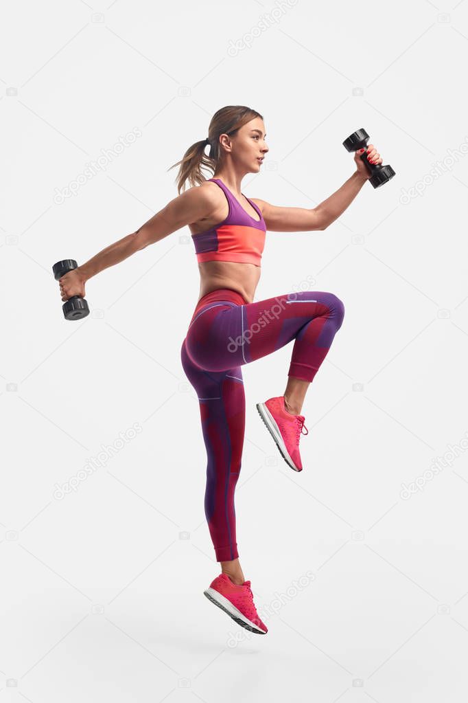 Athletic woman jumping with dumbbells