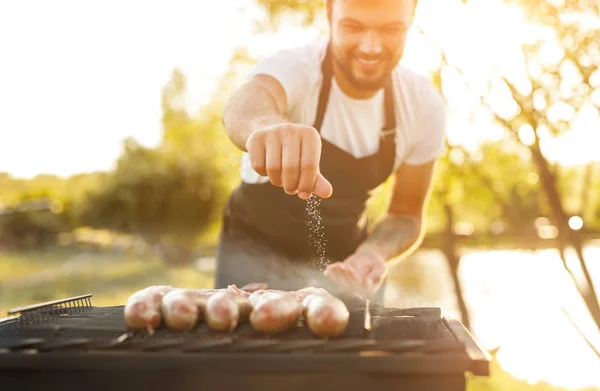 Усміхнений шеф-кухар солять ковбаски на грилі — стокове фото