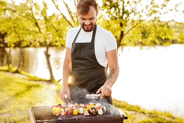 Sorrindo homem preparando shashlik perto do lago — Fotografia de Stock