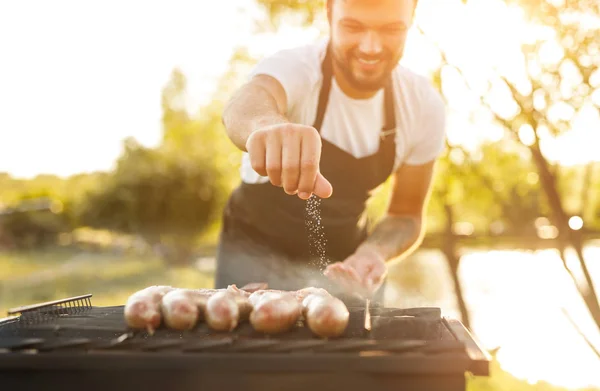 Smiling chef salting sausages on grill — Stock Image Smiling chef salting sausages on grill Royalty Free Stock Photos