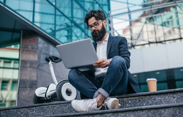 Brodaty przedsiębiorca przy użyciu laptopa w pobliżu gyroscooter — Zdjęcie stockowe