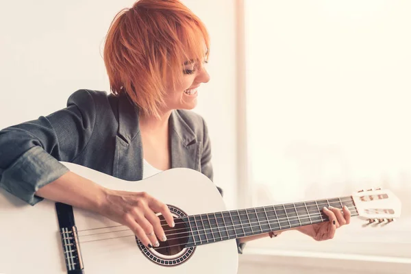 Donna allegra che suona la chitarra vicino alla finestra — Foto Stock