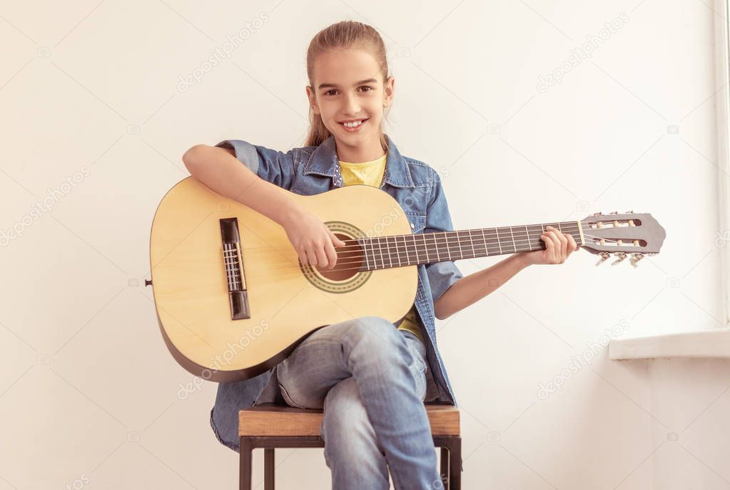 Cheerful girl playing guitar on stool