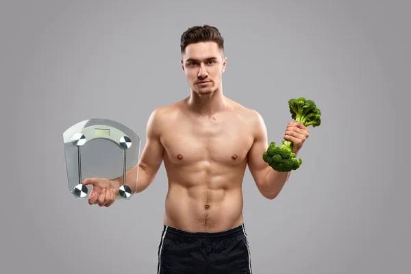 Fit kaslı adam sağlıklı gıda ve ölçekler taşıyan — Stok fotoğraf