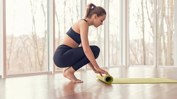 Barefoot woman rolling mat after yoga training — Stock Photo, Image