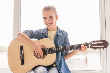 Pencereyakınında gitar çalan gülümseyen çocuk