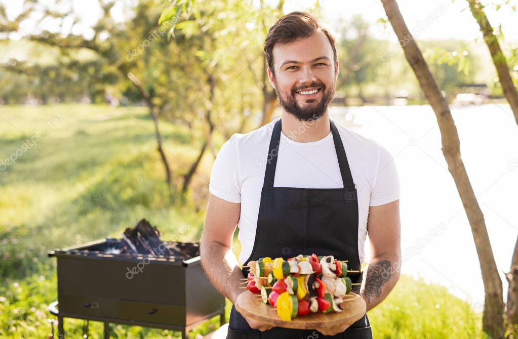 Smiling chef with skewers in nature