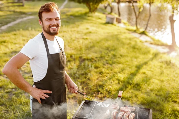 Позитивний чоловік готує м'ясо на грилі — стокове фото