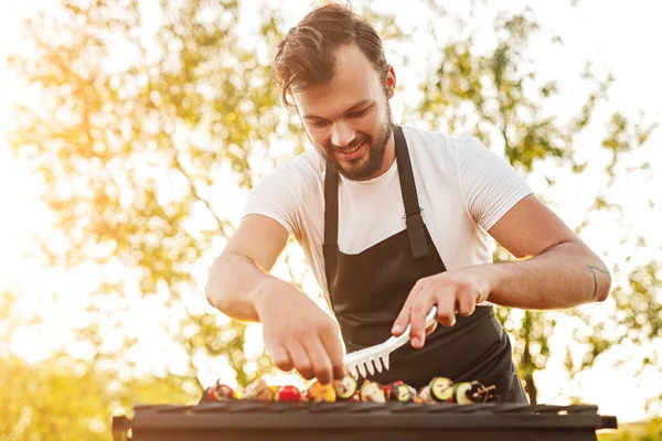 Chef sorridente com pinças preparando espetos na grelha — Fotografia de Stock