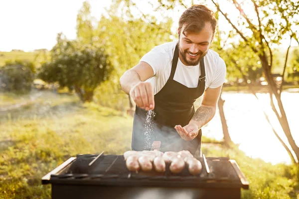 Smiling chef salting sausages on grill — Stock Image Smiling chef salting sausages on grill Stock Picture