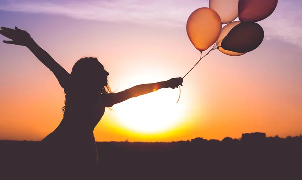 Mulher anônima com balões desfrutando de liberdade durante o pôr do sol — Fotografia de Stock