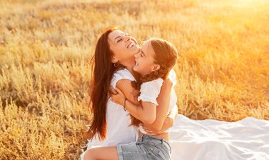 Anne ve kızı sarılma ve beyaz battaniye üzerinde sıcak güneş ışığında gülümseyen