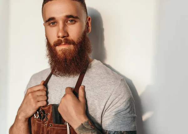 Bearded stylish hairdresser in working apron against wall — Stock Photo, Image