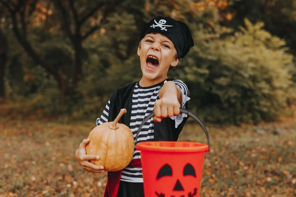 Disguised kid standing with pumpkin and bucket — Stock Photo, Image
