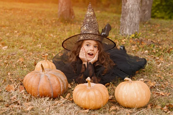 Menina bonito em traje de bruxa deitado com abóboras — Fotografia de Stock