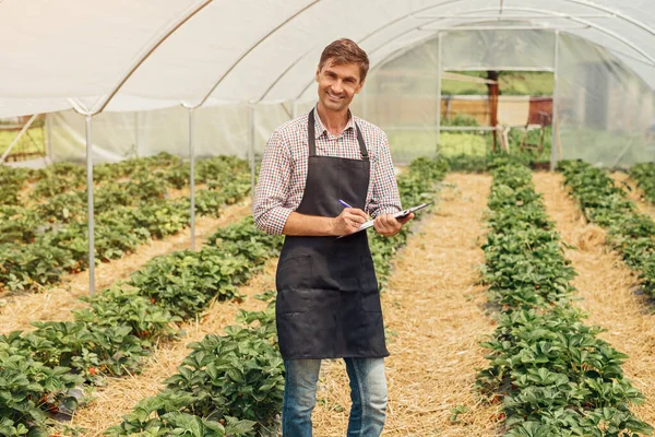 Usmívající se farmář si dělá poznámky ve skleníku — Stock fotografie