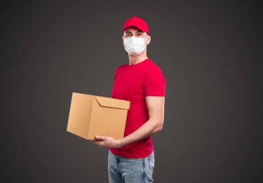 Karton kutu taşıyan maskeli bir teslimatçı.