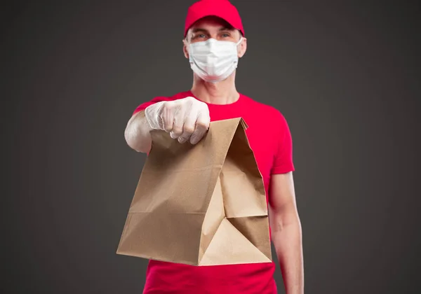 Delivery employee in protective mask and gloves holding bag with order — Stock Photo, Image