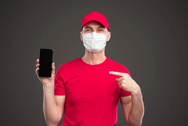 Livrare om în mască de protecție care indică spre smartphone — Fotografie, imagine de stoc