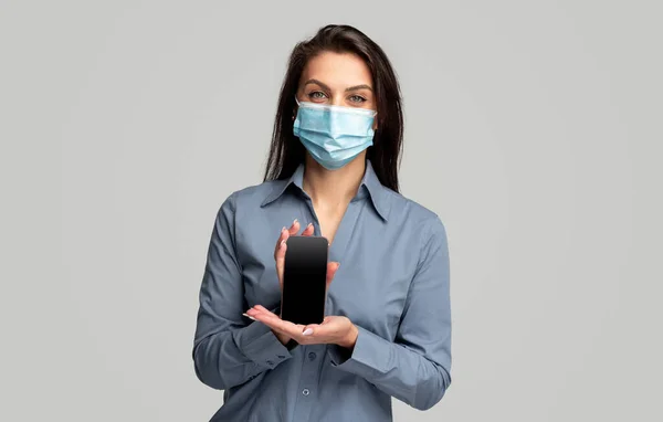 Ung kvinna i medicinsk mask visar smartphone — Stockfoto