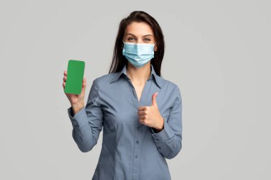 Medikal maskeli kadın akıllı telefon uygulaması reklamı yapıyor.