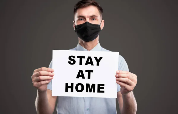 Man in protective mask holding paper with Stay At Home text