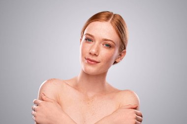 Omuzlarını kucaklayan ve gülümseyen genç bir kadın.