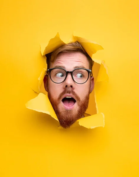 Şaşırmış genç adam kağıttaki delikten bakıyor.