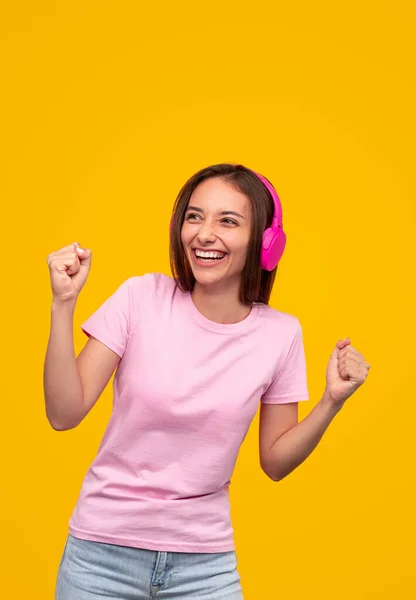 Mujer joven feliz con auriculares rosados escuchando música — Foto de Stock